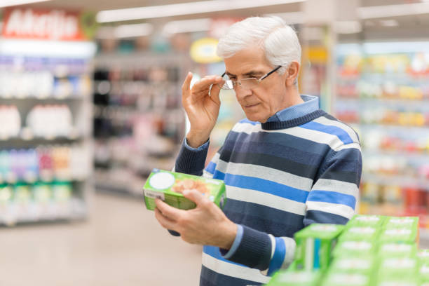 Senior man reading food label at a grocery store Elderly man shopping in local supermarket. He is holding box and reading nutrition label. product review stock pictures, royalty-free photos & images