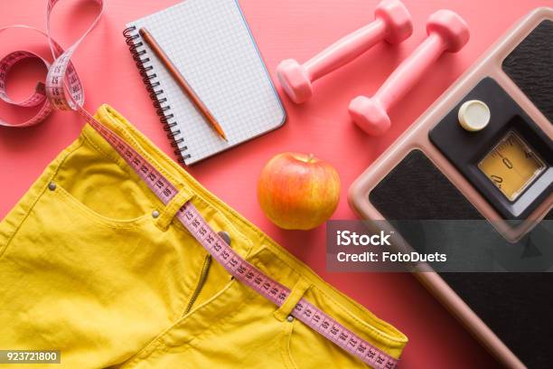 Measure Tape With Yellow Jeans Dumbbells Weight Scale Apple Notebook On A Pink Background Women Diet Before Summer Season Healthy Lifestyle Body Slimming Weight Loss Concept Cares About Body Stock Photo - Download Image Now