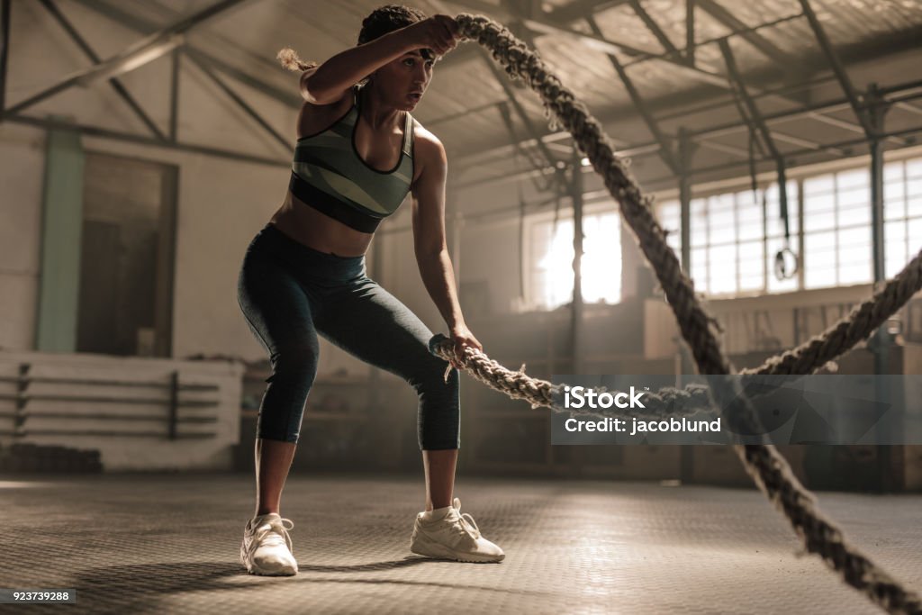 Athlete working out with battle ropes at cross gym Fitness woman using training ropes for exercise at gym. Athlete working out with battle ropes at cross gym. Sports Training Stock Photo