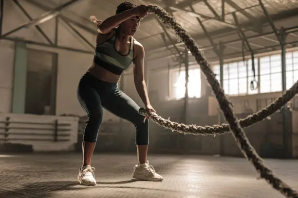 Fitness woman using training ropes for exercise at gym. Athlete working out with battle ropes at cross gym.