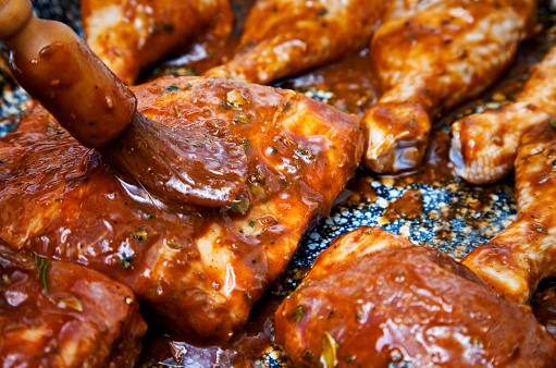 Preparing barbecue meats: pressing marinade into the ribs' every nook and crannies with a brush. Ribs are up front with a row of chicken drumsticks in the background.