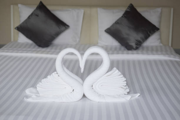 dois cisnes feitos de toalhas formando coração na cama-de-mel suite hotel de quartos decorados para a decoração de preparação do casamento - honeymoon romance wedding bedroom - fotografias e filmes do acervo