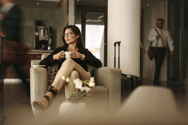 Businesswoman waiting at airport lounge Businesswoman sitting at the airport lounge, waiting for the flight. Thoughtful woman sitting on sofa with coffee at airport waiting area. entrance hall stock pictures, royalty-free photos & images