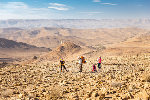 Three backpackers friends tourists hiking standing resting posing arid trail footpath Negev desert mountains traveling, Israel.