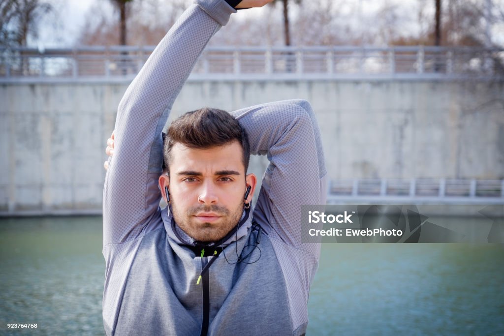 Young athlete man doing sport One young caucasian athlete man is warming up near the river before running in a park Active Lifestyle Stock Photo