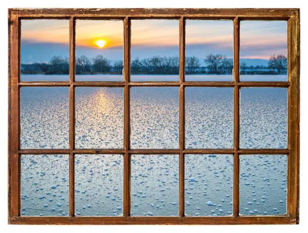 sunset over frozen lake in Colorado as seen through vintage sash window with dirty glass