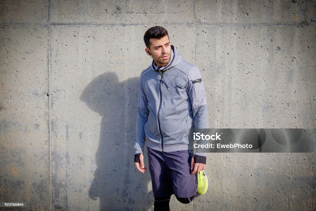 Young athlete man is doing sport runing One young athlete man is resting on a concrete wall after running in a park Active Lifestyle Stock Photo