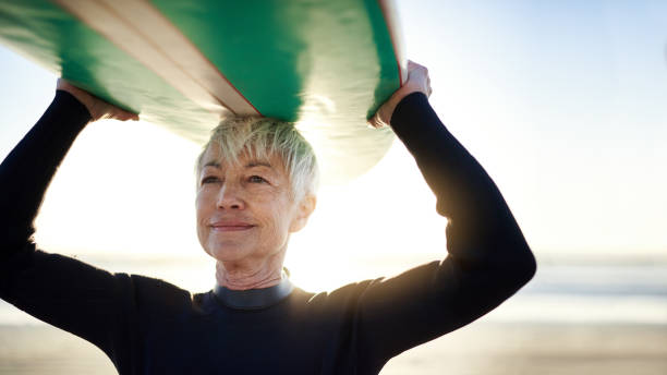 When in doubt, go surfing Cropped shot of a senior woman holding a surfboard on top of her head on her way to go surfing surfing stock pictures, royalty-free photos & images