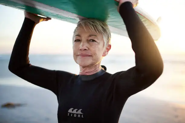 Cropped shot of a senior woman holding a surfboard on top of her head on her way to go surfing