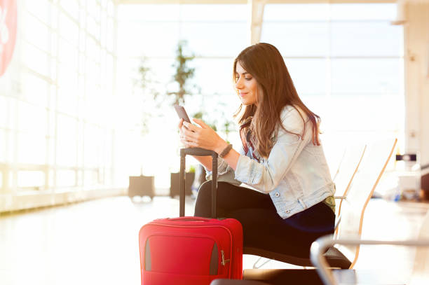 Woman texting and using phone before getting on the plane Casual young woman sitting, using her cell phone while waiting to board a plane at the airport terminal waiting room. airport check in counter photos stock pictures, royalty-free photos & images