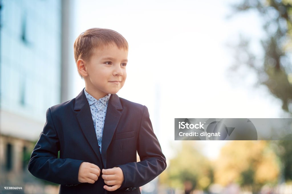 Boy in classic modern dark blue business costume Concept future businessman, president, mayor. Boy in classic dark blue business costume and baby blue shirt walking on pedestrian street, close the jacket button, looking to left. Button - Sewing Item Stock Photo Boy in classic modern dark blue business costume Concept future businessman, president, mayor. Boy in classic dark blue business costume and baby blue shirt walking on pedestrian street, close the jacket button, looking to left. Button - Sewing Item Stock Photo