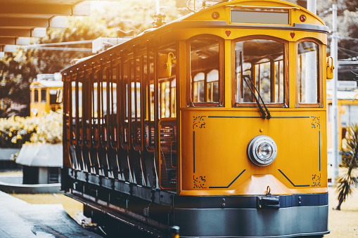 View of empty yellow glossy excursion tram waiting at tramway station in Rio de Janeiro: single headlight, opened interior with wooden windows and seats inside, shallow depth of field, sunny day