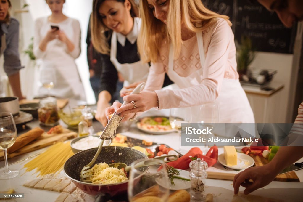 Put some cheese on a pasta Photo of students in a kitchen preparing delicious pasta during a cooking class Cooking Stock Photo