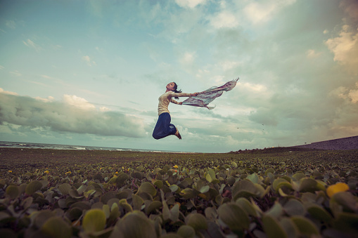 Pretty young women jumping in breezy wind on meadow near beach