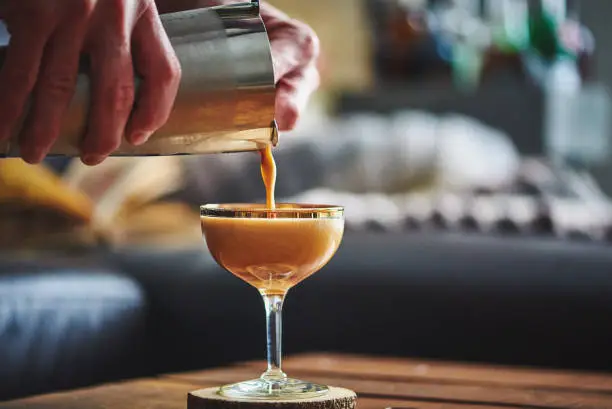 Photo of Male hands pouring espresso martini cocktail into glass