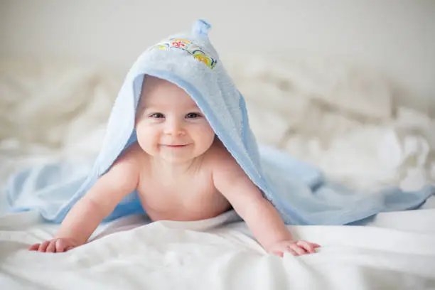 Cute little baby boy, relaxing in bed after bath, smiling happily, daytime