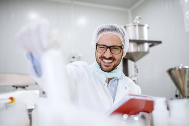 close up of cheerful focused professional happy scientist man holding clipboard and white bottle in the laboratory room. - smiling research science and technology clothing imagens e fotografias de stock