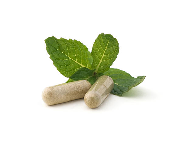 Two capsules and leaves of herbal medicine on white surface stock photo