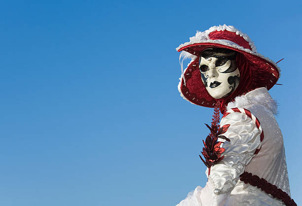 Venice, VE, Italy - February 13, 2024: Masked person with big red hat and luxurious red embroidered dress during the Venetian carnival