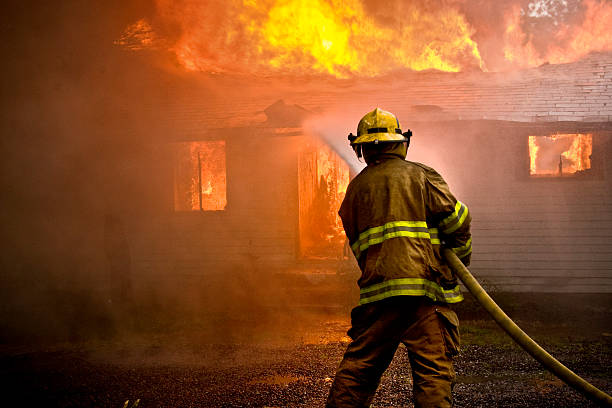 firefighter spraying water at a house fire - brandweer stockfoto's en -beelden