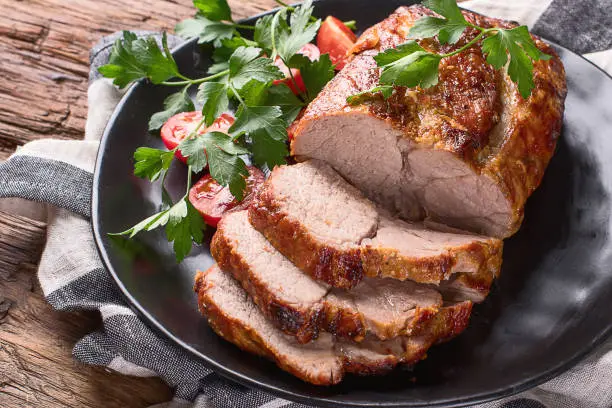 Roast pork with herbs and vegetables on rustic wooden table.