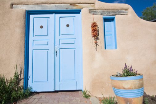 Taos, New Mexico - USA, May 12, 2023. Blue doorway contrasts with earth toned adobe church building in Rancho de Taos New Mexico.
