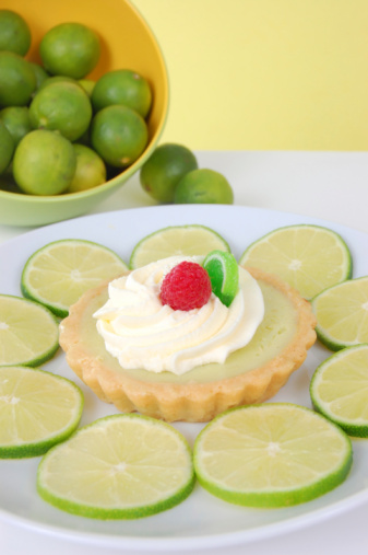 An individual sized key lime tart garnished with a fresh raspberry.