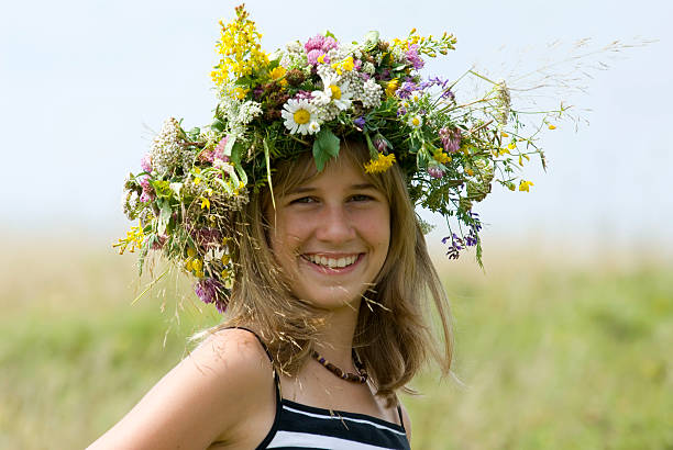 young woman with a flower wreath standing on a meadow, rear view