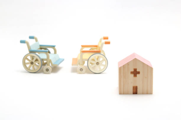 ospedale in legno in miniatura e sedie a rotelle su sfondo bianco. - disablement foto e immagini stock