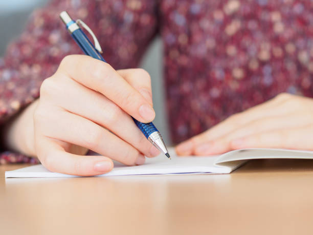 Close up of woman's hands writing in notepad placed on wooden desktop.