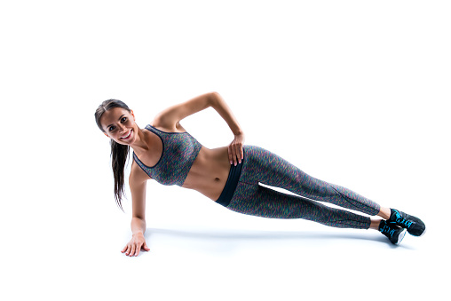 Side profile view photo of happy smiling cheerful sporty flexible young beautiful attractive cute woman clothed in sportive outfit, she is doing plank exercise on one arm, isolated on white background