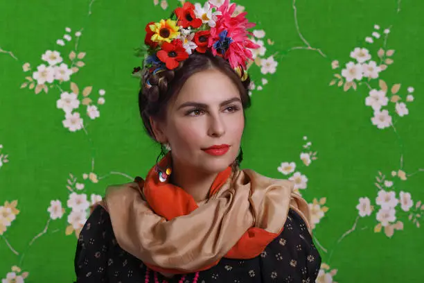 Beautiful young woman with bright red make-up looking like Frida Kahlo. Over green background