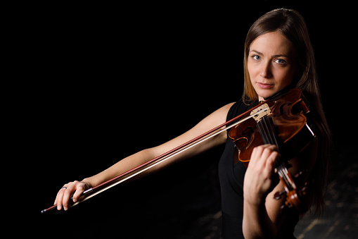 Beautiful young woman playing violin in dark room