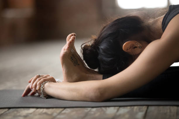 Young woman doing paschimottanasana exercise Young sporty woman practicing yoga, doing paschimottanasana exercise, Seated forward bend pose, working out, wearing black sportswear, indoor close up view, yoga studio knee to the head pose stock pictures, royalty-free photos & images