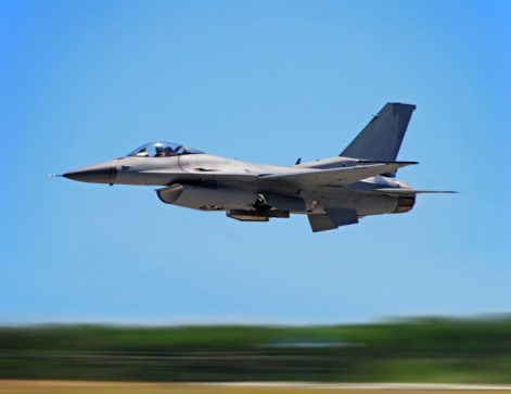 Military figher airplane landing on an airport runway.