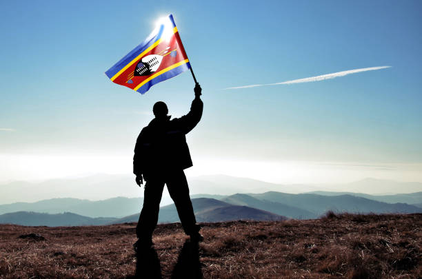 успешный силуэт человека-победителя, размахивающего флагом свазиленда на вершине горной вершины - swaziland стоковые фото и изображения