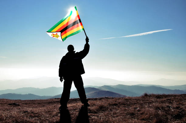Successful silhouette man winner waving Zimbabwe flag on top of the mountain peak stock photo