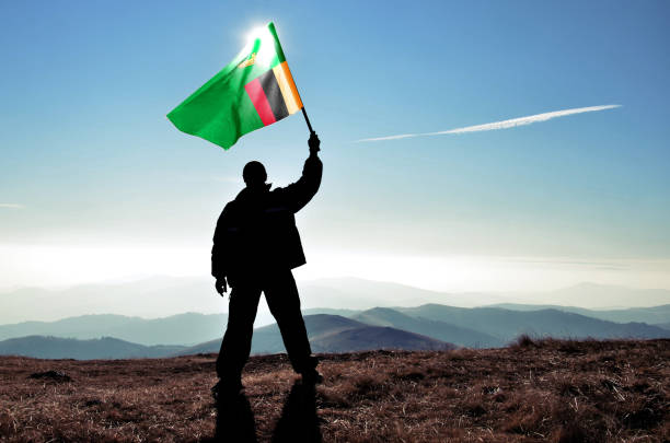 Successful silhouette man winner waving Zambia flag on top of the mountain peak stock photo