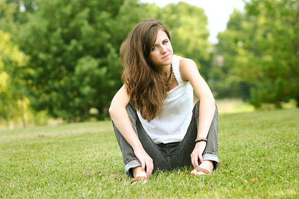 istock Young brunette sitting in grass arms resting on legs 92409401