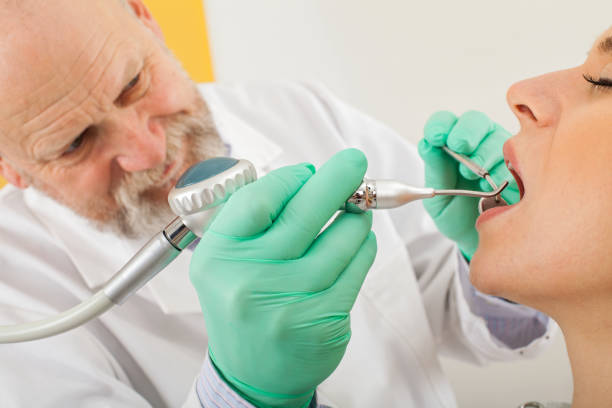 Young handsome dentist examining teeth of happy woman patient sitting on dentist chair in dental clinic. Dentistry care concept.