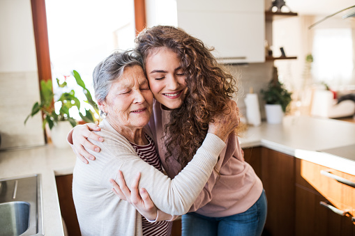 A teenage girl with grandmother at home, hugging. Family and generations concept.