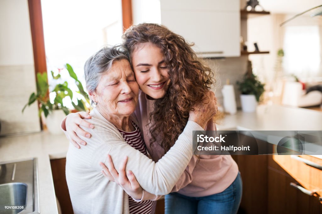A teenage girl with grandmother at home, hugging. A teenage girl with grandmother at home, hugging. Family and generations concept. Grandmother Stock Photo