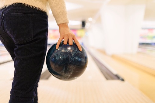 An unrecognizable woman is about to throw a bowling ball.