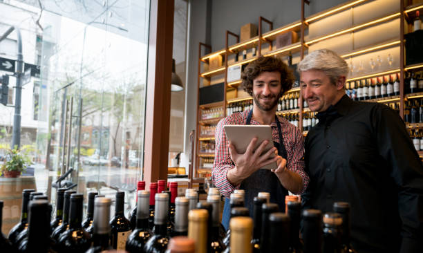 salesman showing a wine app to a customer at a winery both looking very happy and smiling - retail occupation customer advice imagens e fotografias de stock