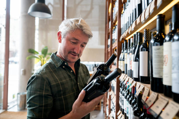 fröhlicher mensch an eine weinhandlung weine auswählen und lesen der etiketten glücklich - wein und spirituosenhandlung stock-fotos und bilder