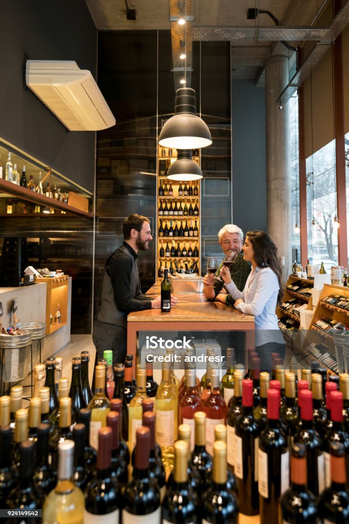 Friendly sommelier teaching a couple about wine tasting at winery Friendly sommelier teaching a couple about wine tasting at winery all looking very happy and smiling Wine Tasting Stock Photo