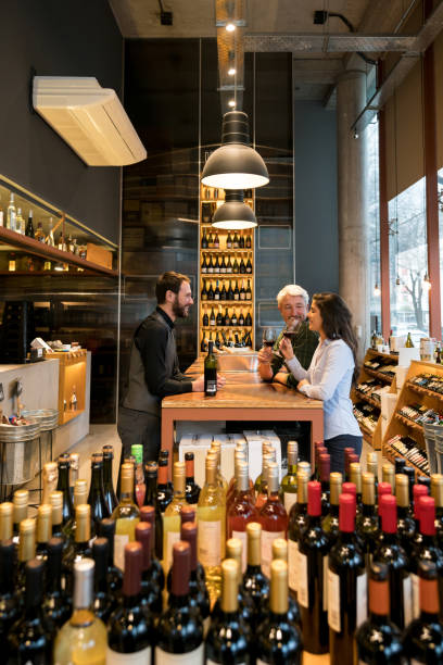 Friendly sommelier teaching a couple about wine tasting at winery Friendly sommelier teaching a couple about wine tasting at winery all looking very happy and smiling bar drink establishment stock pictures, royalty-free photos & images