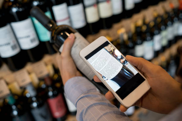 unrecognizable woman using an application on smartphone to read more about the wine - wine bottle liquor store wine variation imagens e fotografias de stock