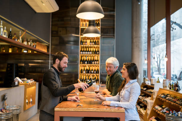 Friendly sommelier serving wine to a couple learning how to taste wine at a winery Friendly sommelier serving wine to a couple learning how to taste wine at a winery all looking very happy and smiling bar drink establishment stock pictures, royalty-free photos & images
