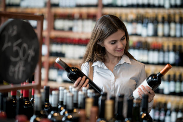 beautiful female customer at a winery buying wine and looking at the labels of the bottles - wine bottle liquor store wine variation imagens e fotografias de stock